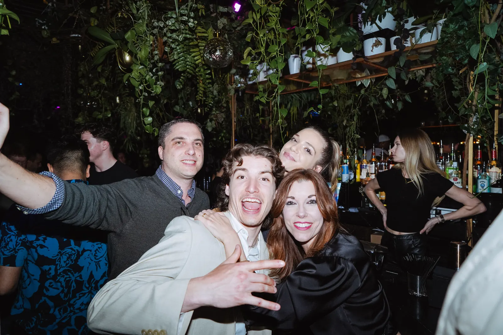 Friends taking a selfie beneath the hanging greenery of The DL rooftop